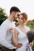 ragazza con un prendisole bianco e un ragazzo con una camicia bianca durante una passeggiata al tramonto con un bouquet foto