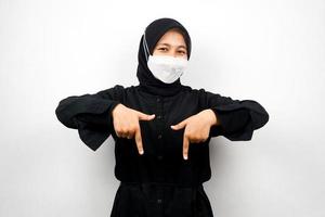 donna musulmana che sorride con sicurezza puntando verso il basso, presentando qualcosa, fare clic sul collegamento sottostante, isolato su sfondo bianco foto