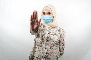 donna musulmana che indossa maschera medica, con la mano del segnale di stop, mano del segno di rifiuto, non mantenere la mano del segno della distanza, non avvicinarsi al segno della mano, isolato su sfondo bianco foto