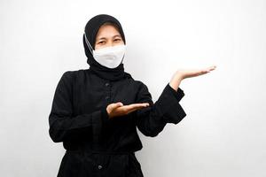 donna musulmana che indossa una maschera bianca, con la mano che punta allo spazio vuoto che presenta qualcosa, isolato su sfondo bianco foto