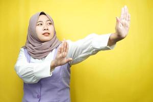 bella giovane donna musulmana asiatica con la mano che rifiuta qualcosa, mano che ferma qualcosa, antipatia per qualcosa nello spazio vuoto, isolato su sfondo giallo foto
