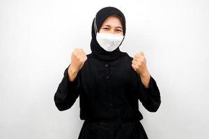 donna musulmana che indossa maschera bianca, pugni chiusi, pugni con le mani, mani segno di vittoria, spirito, prevenire il virus corona, prevenire covid-19, isolato su sfondo bianco foto