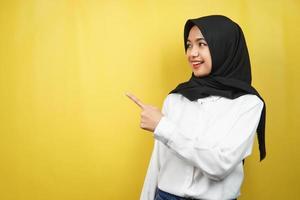 bella giovane donna musulmana asiatica con le mani che puntano lo spazio vuoto che presenta qualcosa, sorridente fiducioso, entusiasta, allegro, di fronte allo spazio vuoto, isolato su sfondo giallo foto