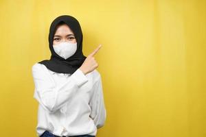 donna musulmana che indossa una maschera bianca, con la mano che punta allo spazio vuoto che presenta qualcosa, isolato su sfondo giallo foto