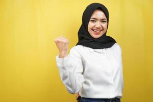 bella giovane donna musulmana asiatica sorridente sicura di sé, entusiasta e allegra con le mani serrate, segno di successo, pugni, combattimento, non paura, vittoria, isolato su sfondo giallo