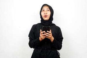 bella giovane donna musulmana asiatica scioccata, sorpresa, espressione wow, mano che tiene lo smartphone, guardando in alto, isolato su sfondo bianco