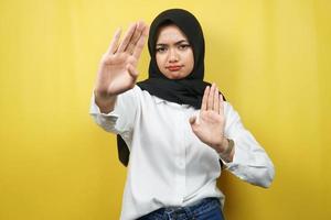 bella giovane donna musulmana asiatica con la mano del segnale di stop, rifiutare la mano del segno, mano del segnale di divieto, non avvicinarsi alla mano, stare lontano dalla mano del segno, non muovere la mano del segno, isolata su sfondo giallo foto
