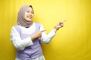 bella giovane donna musulmana asiatica sorridente sicura di sé, entusiasta e allegra con le mani che puntano lo spazio vuoto presentando qualcosa di fronte alla telecamera isolata su sfondo giallo, concetto di pubblicità foto