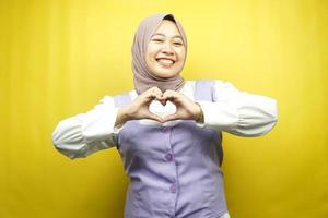 bella giovane donna musulmana asiatica sorridente sicura di sé, entusiasta e allegra con le mani segno di amore, affetto, felice, sul petto isolato su sfondo giallo foto
