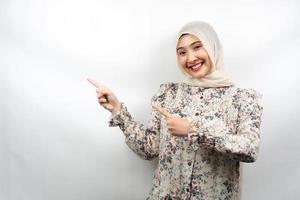 bella giovane donna musulmana asiatica sorridente sicura di sé, entusiasta e allegra con le mani che puntano lo spazio vuoto presentando qualcosa di fronte alla telecamera isolata su sfondo bianco, concetto di pubblicità foto