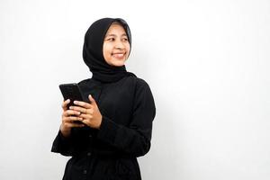 bella giovane donna musulmana asiatica con le mani che tengono lo smartphone, sorridente fiducioso, entusiasta e allegro, vista guardando lo spazio vuoto che presenta qualcosa, isolato su sfondo bianco