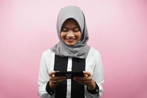 bella giovane donna musulmana asiatica con le mani che tengono smartphone, gioco, sorridente felicemente, vittoria, successo, isolato su sfondo rosa, concetto pubblicitario