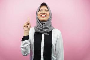 bella giovane donna musulmana asiatica sorridente sicura di sé, entusiasta e allegra con le mani rivolte verso l'alto, ottenere idee, trovare soluzioni, presentare qualcosa, isolato su sfondo rosa