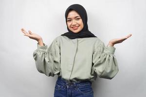 bella giovane donna musulmana asiatica sicura e sorridente, a braccia aperte, che presenta qualcosa, presenta un prodotto, isolata su sfondo grigio foto