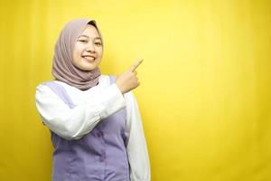 bella giovane donna musulmana asiatica con le mani che puntano lo spazio vuoto che presenta qualcosa, sorridente fiducioso, entusiasta, allegro, guardando la telecamera, isolato su sfondo giallo