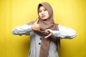 Bella asiatica giovane donna musulmana con segno di mano come o antipatia, sì o no, felice o triste, confrontando due cose, isolato su sfondo giallo