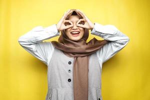 bella giovane donna musulmana asiatica che sorride allegramente ed eccitata, con le mani degli occhiali, isolata su sfondo giallo