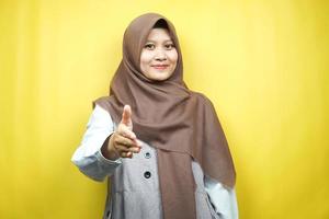 bella giovane donna musulmana asiatica sorridente con fiducia, con le mani che stringono la macchina fotografica, segno di cooperazione con le mani, segno di accordo con la mano, segno di amicizia con la mano, isolato su sfondo giallo