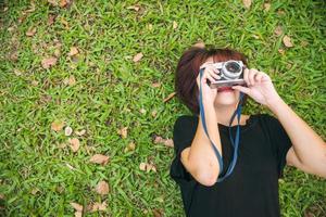 primo piano di una giovane donna asiatica sdraiata sull'erba verde fredda e scatta una foto con la sua macchina fotografica. giovane donna rilassante sull'erba con la sua macchina fotografica accanto. attività all'aperto nel concetto di parco.