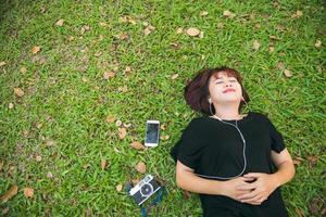 giovane donna asiatica sdraiata sull'erba verde ascoltando musica nel parco con un'emozione gelida. giovane donna che si rilassa sull'erba con la sua playlist musicale. attività all'aperto nel concetto di parco.