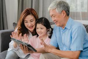 nonni asiatici e videochiamata nipote a casa. cinese anziano, nonno e nonna felici con la ragazza che utilizza la videochiamata del telefono cellulare parlando con papà e mamma sdraiati nel soggiorno di casa. foto