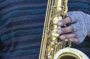 la mano di un musicista senzatetto in guanti su un sassofono. foto