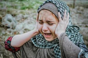 un bambino rifugiato in guerra, una ragazza musulmana con la faccia sporca sulle rovine, il concetto di pace e guerra, il bambino piange e aspetta aiuto. foto