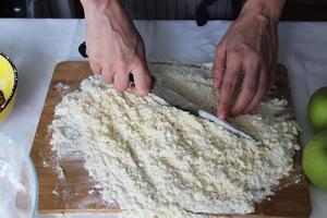 le mani del cuoco tritano burro e farina su una tavola di legno con un coltello. Torta fatta in casa. lavori di casa. foto