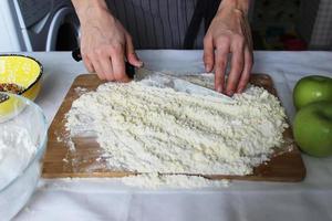 le mani del cuoco tritano burro e farina su una tavola di legno con un coltello. Torta fatta in casa. lavori di casa. foto