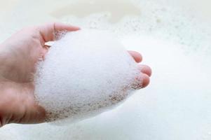 schiuma di sapone sulla mano di una persona su uno sfondo di schiuma di sapone. il concetto di pulizia e igiene. foto
