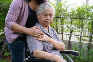 la figlia del caregiver aiuta la donna anziana anziana o anziana asiatica su sedia a rotelle elettrica nel parco. foto