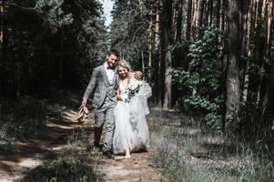 gli sposi attraversano il bosco abbracciati. sposa a piedi nudi, lo sposo porta le scarpe. giornata di sole estivo. foto