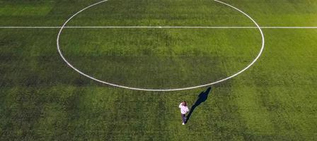 una ragazzina adolescente corre rapidamente attraverso il campo di calcio dello stadio per lottare per la vittoria sparando da una vista a volo d'uccello con un drone foto