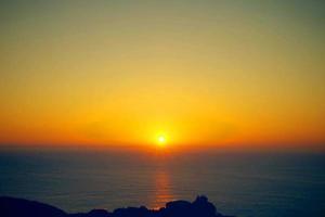tramonto arancione in mare e cielo blu bellissimo mare e tramonto con un grande sole giallo sotto le colline della superficie del mare sullo sfondo. foto