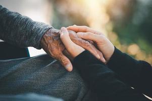la mano di una giovane donna che abbraccia la mano degli anziani concetto di assistenza, cura delle famiglie, cura degli anziani foto