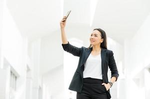 donna lavoratrice asiatica che tiene un telefono cellulare in piedi in ufficio donna che lavora concetto donna d'affari in aula tecnologia foto