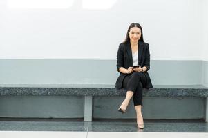 donna lavoratrice asiatica che tiene un telefono cellulare in piedi in ufficio donna che lavora concetto donna d'affari in aula tecnologia foto