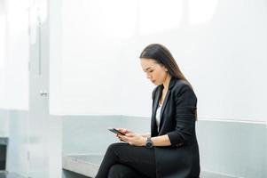 donna lavoratrice asiatica che tiene un telefono cellulare in piedi in ufficio donna che lavora concetto donna d'affari in aula tecnologia foto