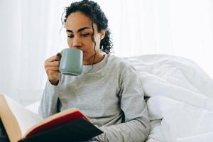 donna africana concentrata che beve caffè e legge un libro foto