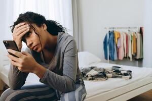 giovane donna di colore che usa il cellulare mentre è seduta sul letto foto