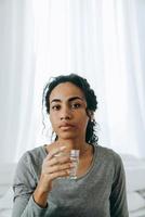giovane donna di colore che beve acqua durante il tempo a casa foto
