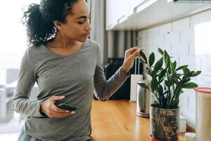 donna di colore che usa il cellulare mentre si trova in cucina foto