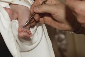 il prete spalma d'olio la gamba del bambino alla cerimonia del battesimo in chiesa. religione. avvicinamento. foto