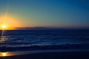 tramonto arancione in mare e cielo blu bellissimo mare e tramonto con un grande sole giallo sotto le colline della superficie del mare sullo sfondo. foto
