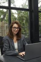 giovane donna nel occhiali Lavorando con il computer portatile mentre seduta a bar foto