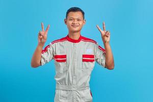 ritratto di giovane meccanico asiatico sorridente che fa segno di pace con il dito isolato su sfondo blu foto