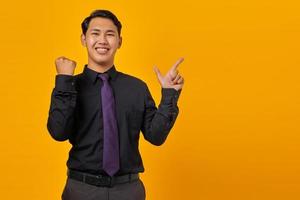 ritratto di giovane uomo d'affari asiatico sorridente che punta il dito sullo spazio della copia e celebra la vittoria su sfondo giallo