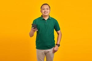 ritratto di giovane uomo asiatico sorridente che tiene il telefono cellulare su sfondo giallo foto