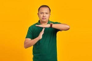 ritratto di un bell'uomo asiatico che mostra il gesto del limite di tempo su sfondo giallo foto