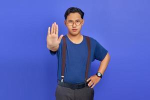 ritratto di un bel giovane che indossa una maglietta blu che sembra arrabbiato e fa un gesto di arresto con le palme su sfondo viola foto